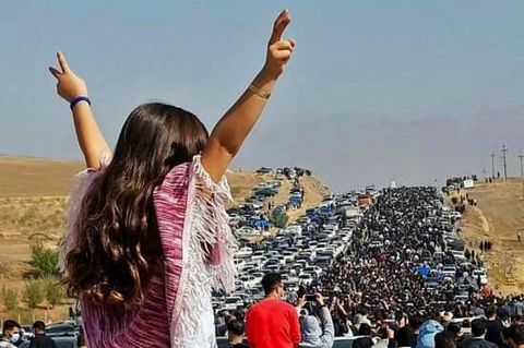 Eine Frau im Iran steht ohne Kopftuch auf einem Auto und macht mit beiden Händen ein Victory-Zeichen