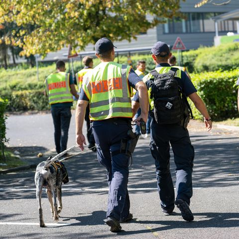 Mit einem Spürhund durchsuchen Polizeibeamte das Gebiet am Schulzentrum in Lohr am Main