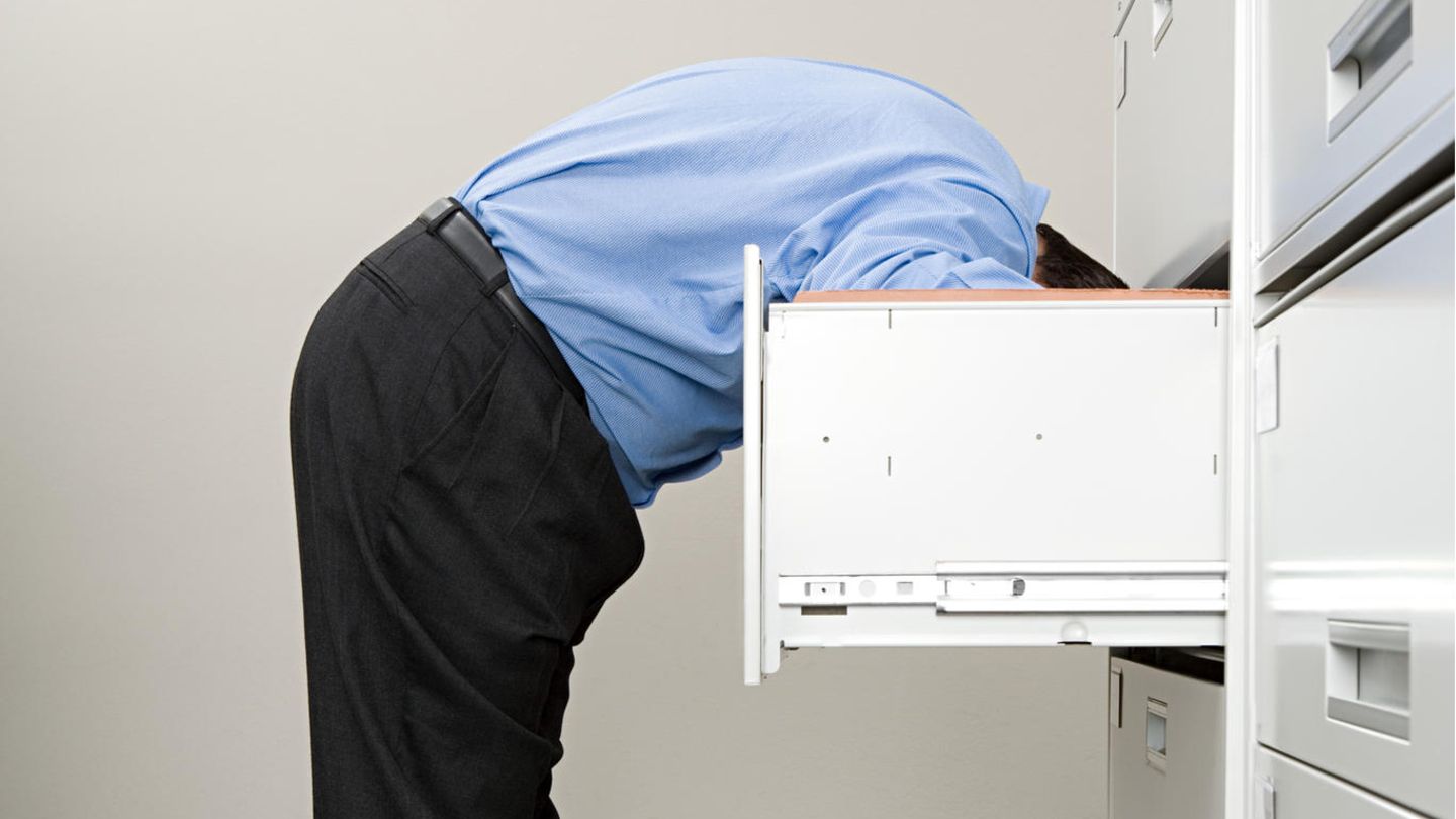 Mann sucht kopfüber etwas in einem Schrank (Symbolbild)