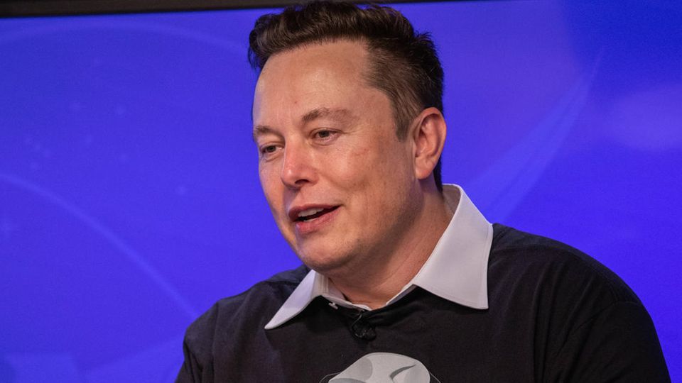 Elon Musk ssitzt auf einem Stuhl auf einem Podium