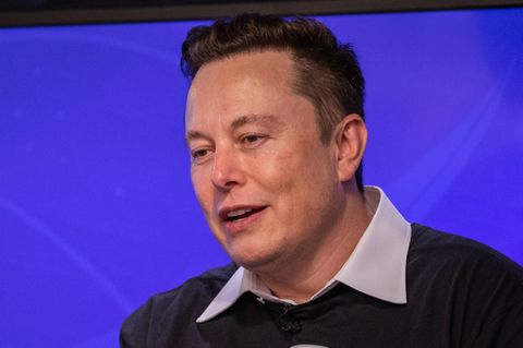 Elon Musk ssitzt auf einem Stuhl auf einem Podium