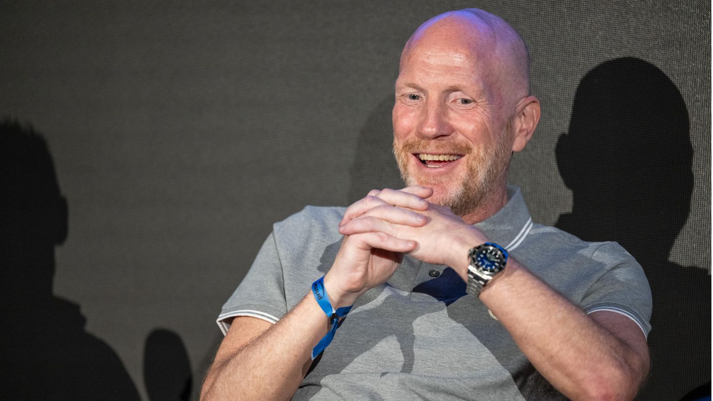 Matthias Sammer sitzt und lacht bei einer Pressekonferenz