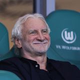 Rudi Völler sitzt auf einer Bank und lacht