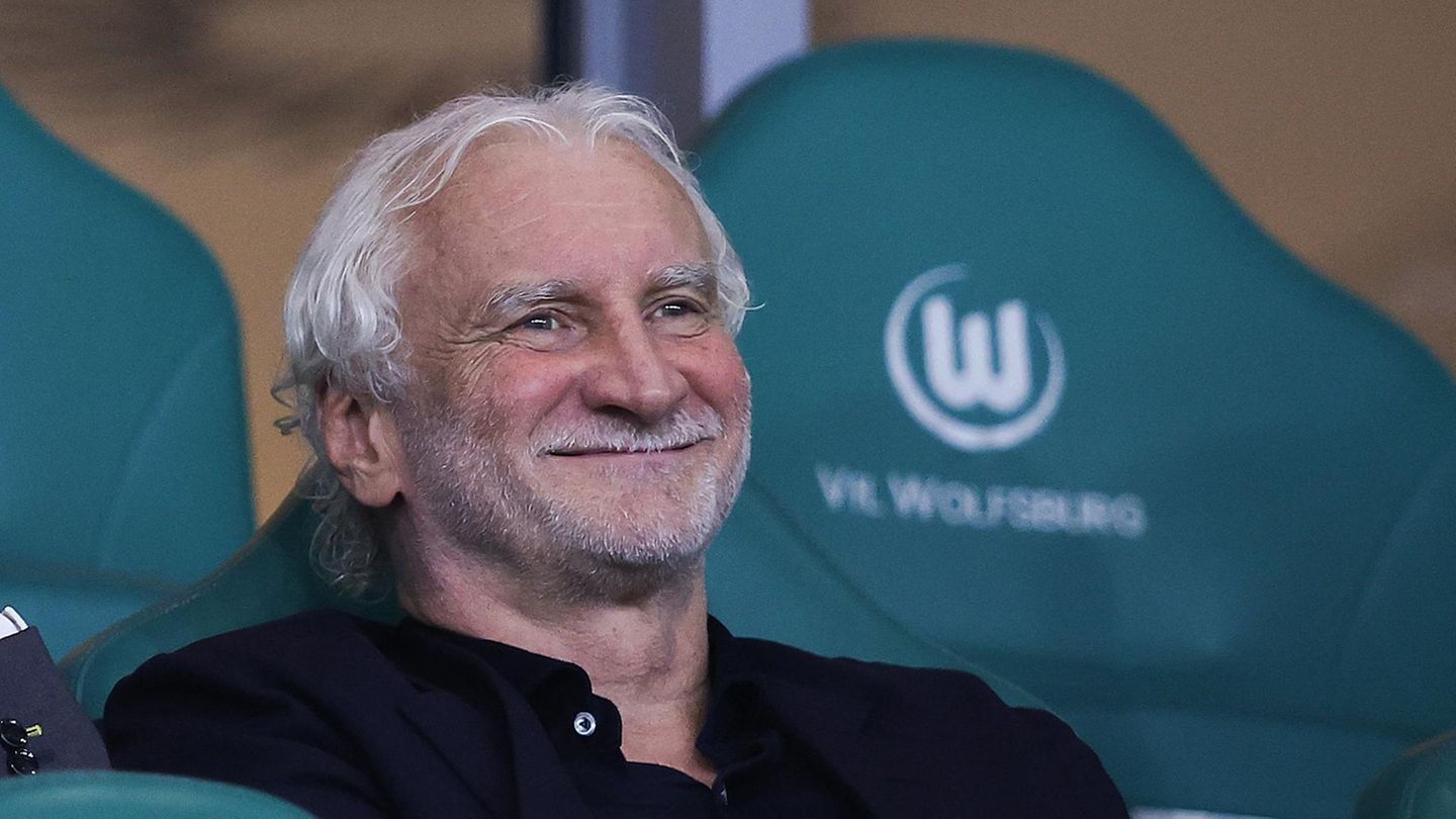 Rudi Völler sitzt auf einer Bank und lacht