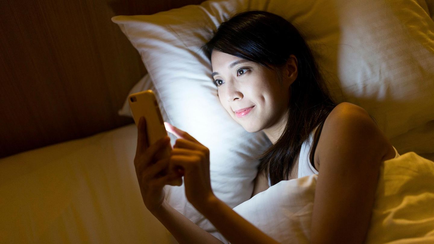 Eine Frau liegt im Bett und tippt auf ihrem Smartphone Eine Frau liegt im Bett und tippt auf ihrem Smartphone