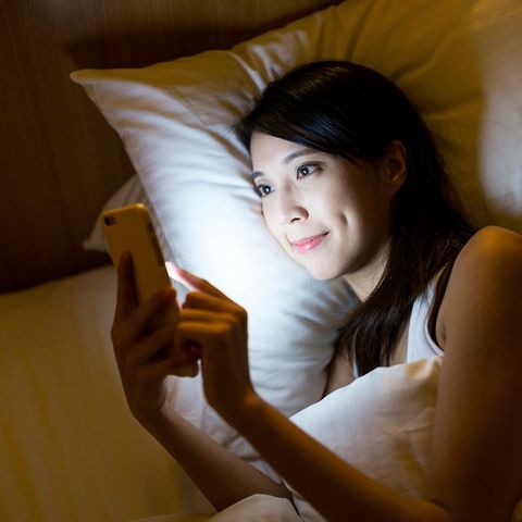 Eine Frau liegt im Bett und tippt auf ihrem Smartphone