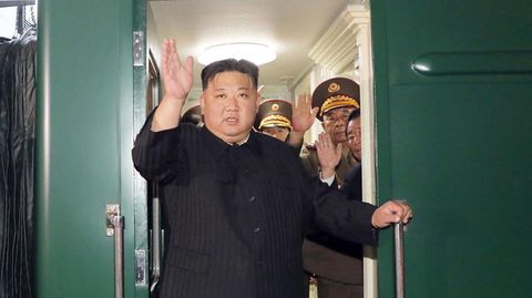 Kim Jong Un steht in einer Tür seines Panzerzuges und winkt mit rechts, während er sich mit links festhält