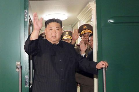 Kim Jong Un steht in einer Tür seines Panzerzuges und winkt mit rechts, während er sich mit links festhält