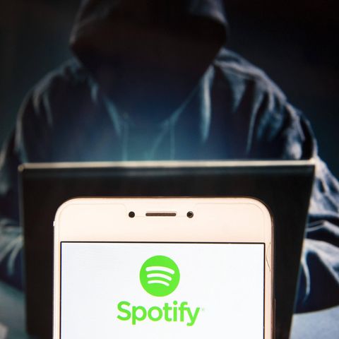 Das Spotify-Logo auf einem Smartphone-Bildschirm mit einer dahintersitzenden Person, die eine Kapuze trägt