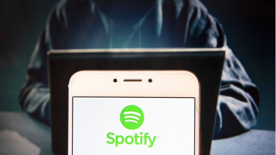 Das Spotify-Logo auf einem Smartphone-Bildschirm mit einer dahintersitzenden Person, die eine Kapuze trägt