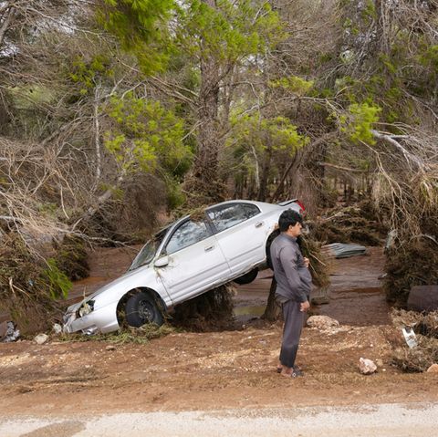 Ein Mann steht in der überfluteten Stadt Darna in Libyen neben einem weggeschwemmten Auto