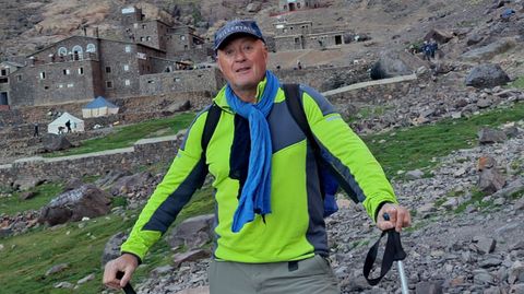 Der 60-jährige Winfried Friedel steht mit Wanderstöcken vor einem Bergdorf im Hohen Atlas