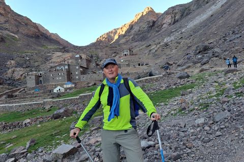 Der 60-jährige Winfried Friedel steht mit Wanderstöcken vor einem Bergdorf im Hohen Atlas
