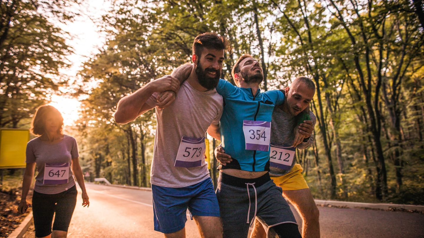 Zwei Sportler helfen einem verletzten Kontrahenten über die Ziellinie Zwei Sportler helfen einem verletzten Kontrahenten über die Ziellinie