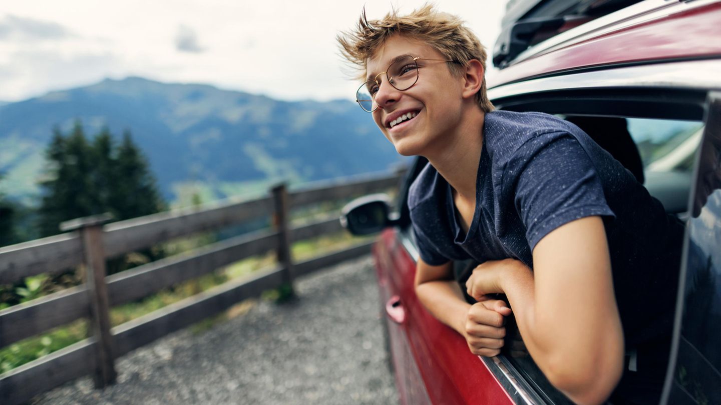 Ein junger Mann lehnt sich aus dem Autofenster und blickt zufrieden in die Landschaft