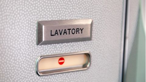 Die grau-weiß gepunktete Tür einer Flugzeugtoilette ist mit einem "Lavatory"-Schild gekennzeichnet und gerade geschlossen