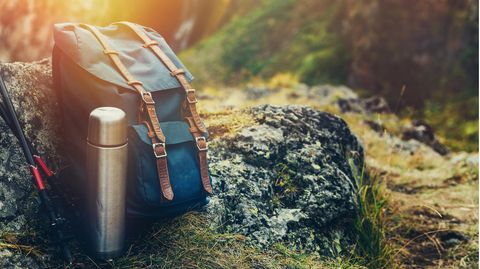Deals und Angebote: Rucksack, Thermosflasche und Stöcke liegen in der Abendsonne auf einem Felsen