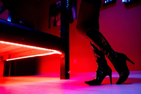 Die Beine einer Prostituierten in Deutschland neben dem Bett. Sie trägt hochhackige Stiefel