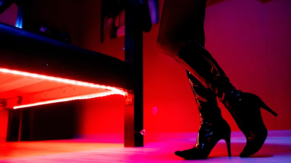 Die Beine einer Prostituierten in Deutschland neben dem Bett. Sie trägt hochhackige Stiefel