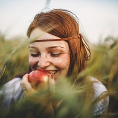 Eine Frau steht im Feld und isst einen Apfel