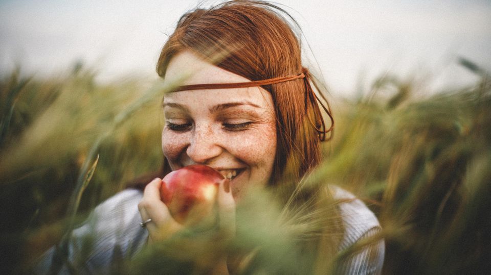 Eine Frau steht im Feld und isst einen Apfel