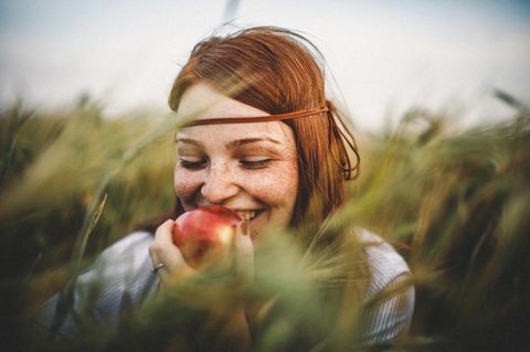 Eine Frau steht im Feld und isst einen Apfel
