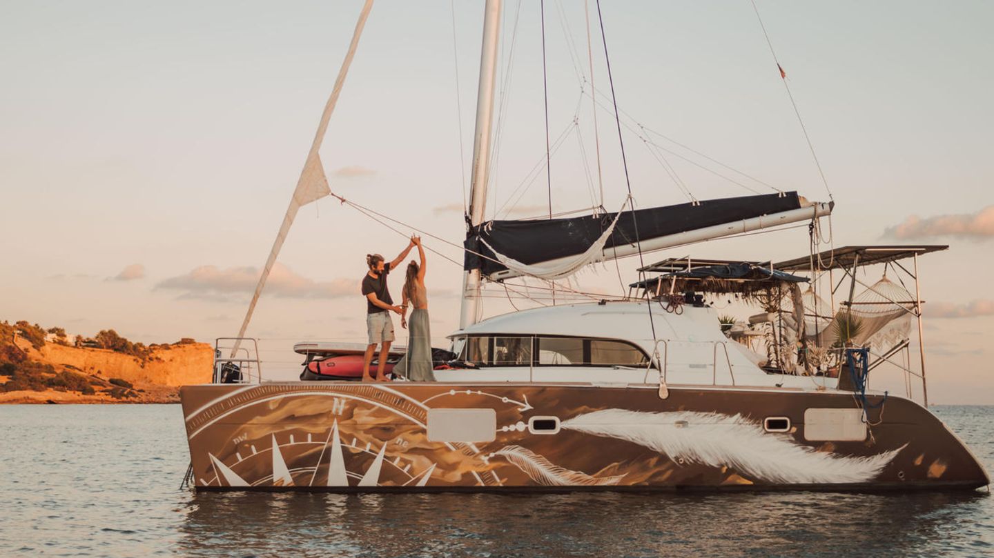 Ein Paar tanzt auf seinem Katamaran, der in einer Bucht liegt