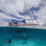 Ein Segelboot liegt im Wasser, davor sieht man, wie ein Mensch taucht