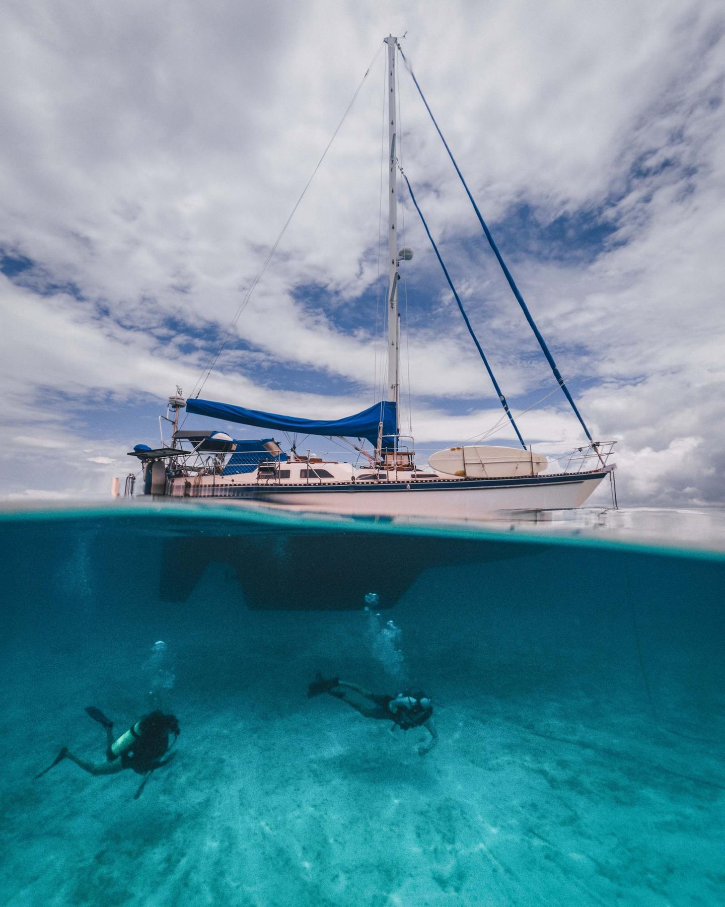 Ein Segelboot liegt im Wasser, davor sieht man, wie ein Mensch taucht Ein Segelboot liegt im Wasser, davor sieht man, wie ein Mensch taucht