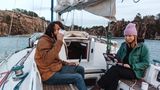 Ein Paar sitzt an Bord seines Segelschiffes, er trinkt Kaffee, sie arbeitet auf dem Laptop
