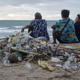 Menschen sitzen vor einem Haufen Plastikmüll am Strand von Bali