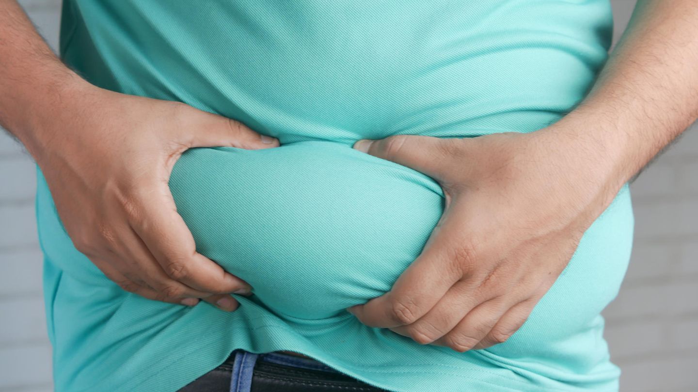 Übergewicht: Mann im T-Shirt hält seinen adipösen Bauch mit beiden Händen Übergewicht: Mann im T-Shirt hält seinen adipösen Bauch mit beiden Händen