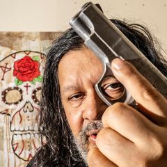 Alfredo Martinez hält sich eine Pistole vor das Gesicht und guckt mit einem Auge am Abzug vorbei