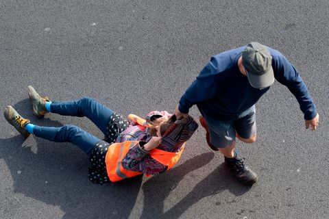 Ein Verkehrsteilnehmer zieht bei einer Blockade der Letzten Generation eine Aktivistin von der Straße