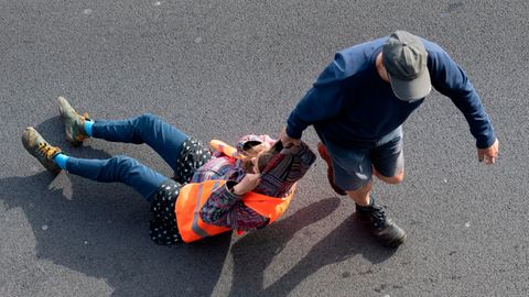 Ein Verkehrsteilnehmer zieht bei einer Blockade der Letzten Generation eine Aktivistin von der Straße