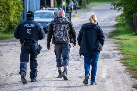 Ein Polizist und eine Polizistin gehen neben einem Skinhead durch Jamel in Mecklenburg-Vorpommern