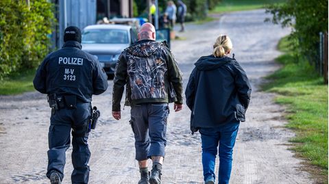 Ein Polizist und eine Polizistin gehen neben einem Skinhead durch Jamel in Mecklenburg-Vorpommern