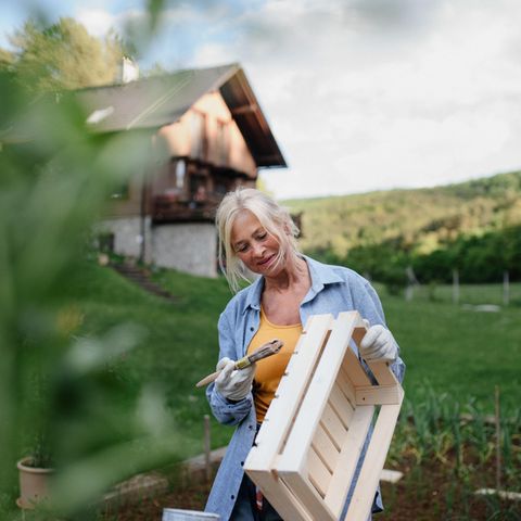 Eine ältere Frau streicht eine Holzkiste