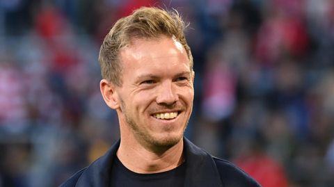 Julian Nagelsmann, schwarzes T-Shirt, schwarzer Mantel, lacht am Spielfeldrand