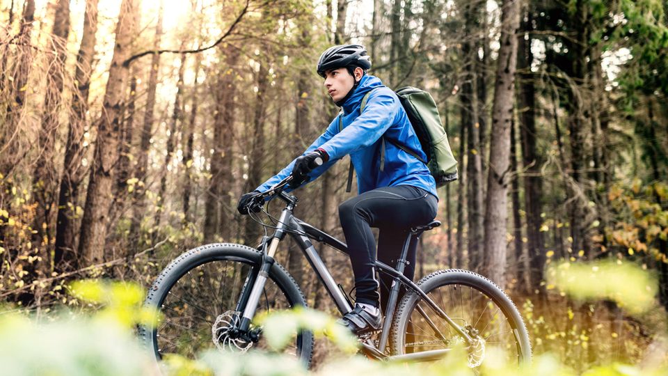 Radmode für Männer: Mountainbiker im Wald mit Rucksack