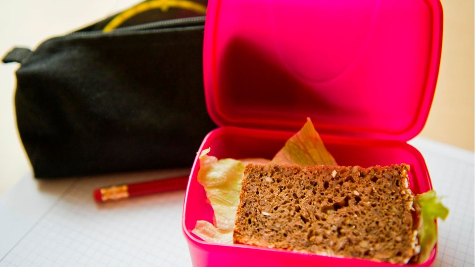 Ein Vollkornbrot mit Salat liegt in einer Brotdose neben einer Federmappe