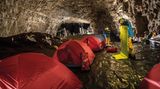 Rote Zelte und zwei Männer in gelben Hose und hellblauen Jacken in einer Höhle