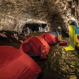 Rote Zelte und zwei Männer in gelben Hose und hellblauen Jacken in einer Höhle