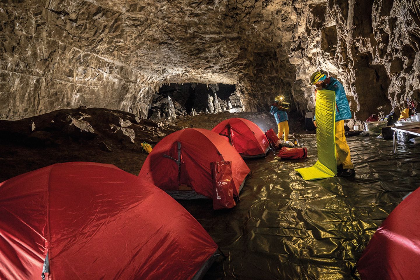Rote Zelte und zwei Männer in gelben Hose und hellblauen Jacken in einer Höhle