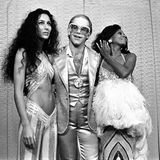Cher und Diana Ross rahmen Elton John ein, der eine große Brille trägt