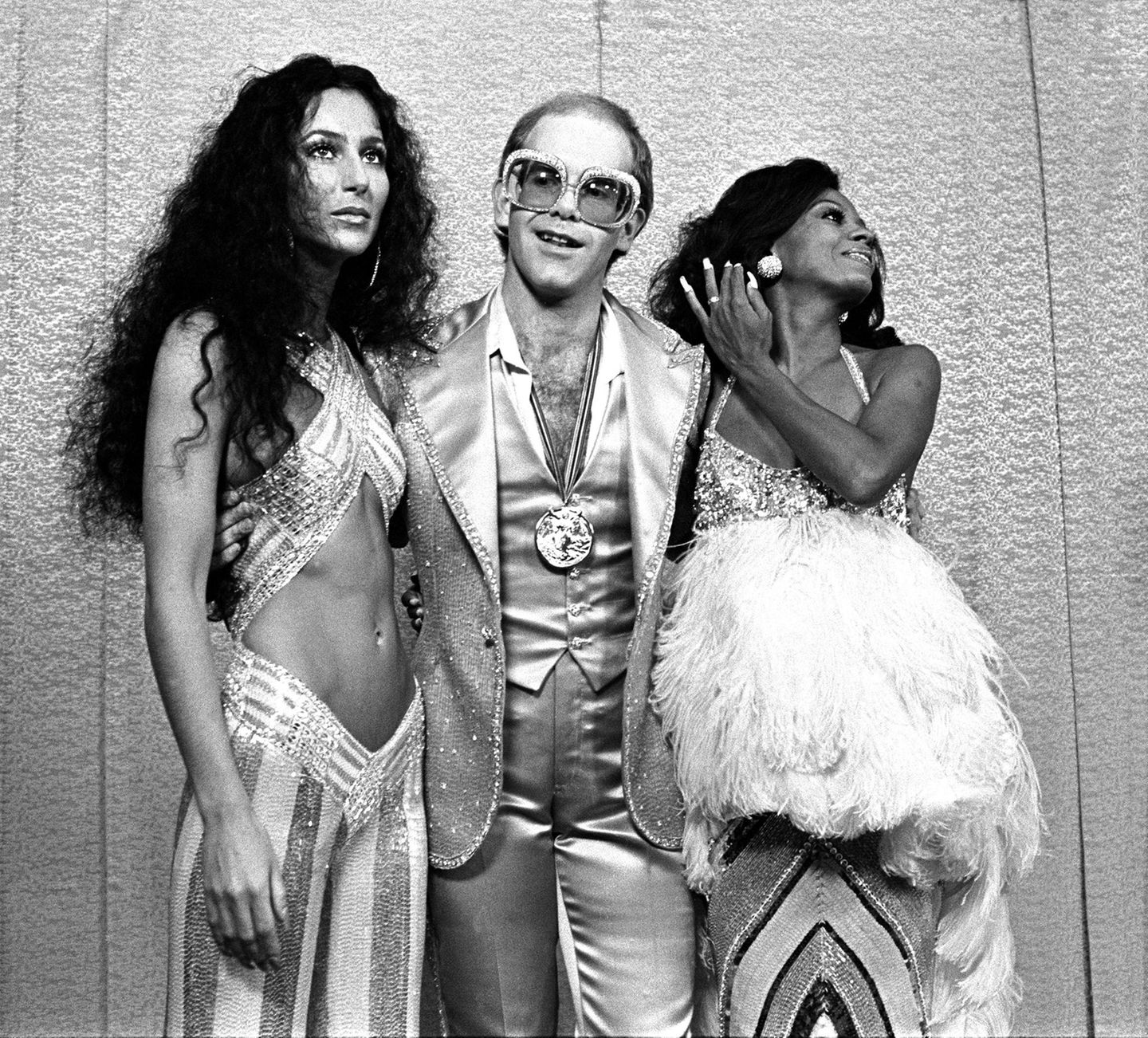Cher und Diana Ross rahmen Elton John ein, der eine große Brille trägt