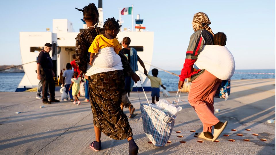 zwei Frauen tragen ihre Kinder auf dem Rücken und ihr Gepäck zur Fähre von Lampedusa