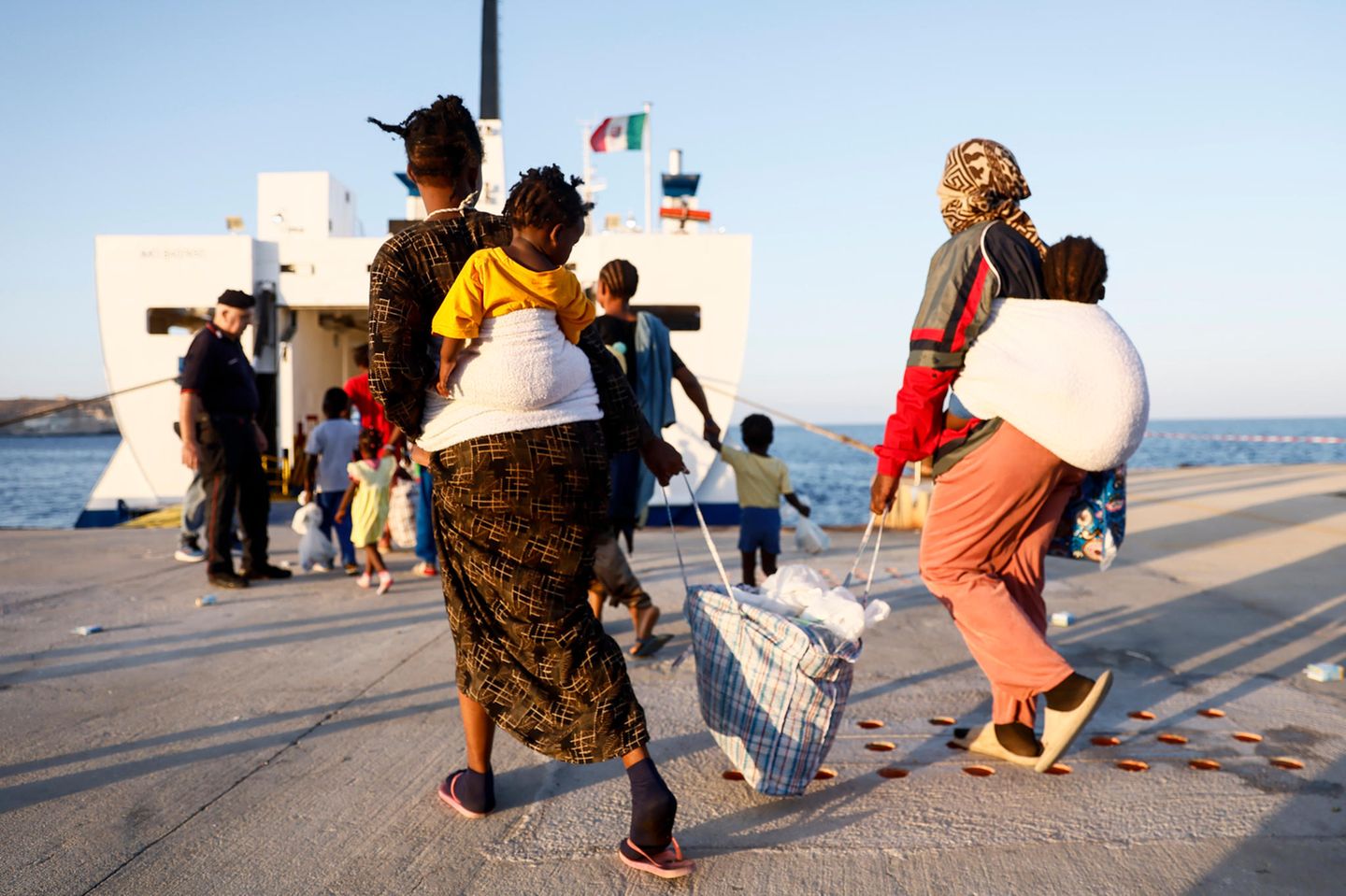 zwei Frauen tragen ihre Kinder auf dem Rücken und ihr Gepäck zur Fähre von Lampedusa