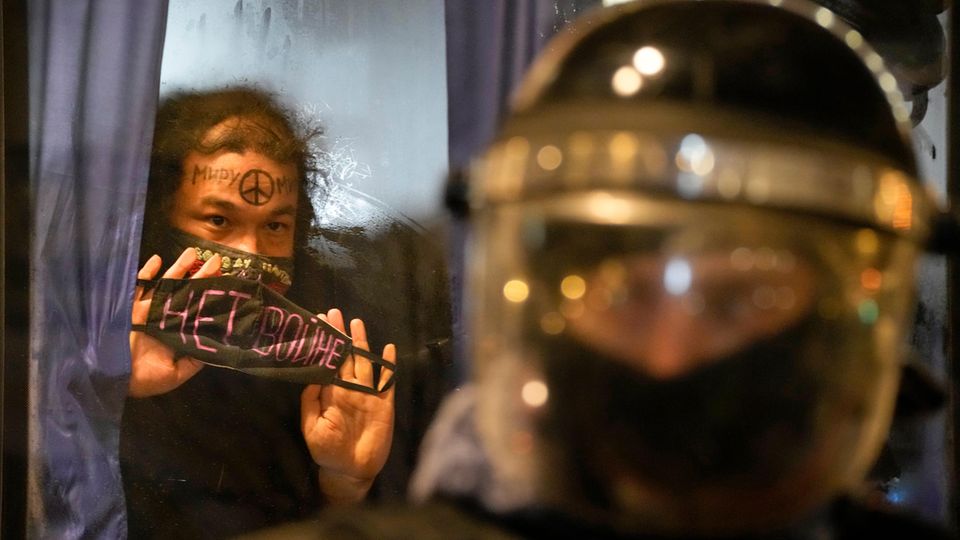 Ein festgenommener Demonstrant zeigt aus einem Polizeibus in Schild mit der Aufschrift "Kein Krieg!"