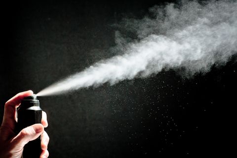 Vor schwarzem Hintergrund schiept ein Strahl Spray aus einer Deodorant-Sprühdose